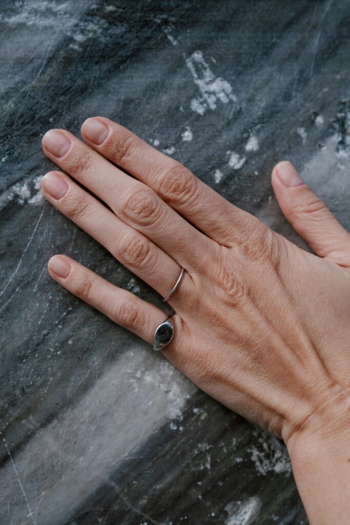 pexels photo 6328440 6328440 A woman's hand adorned with rings resting on a textured marble surface.